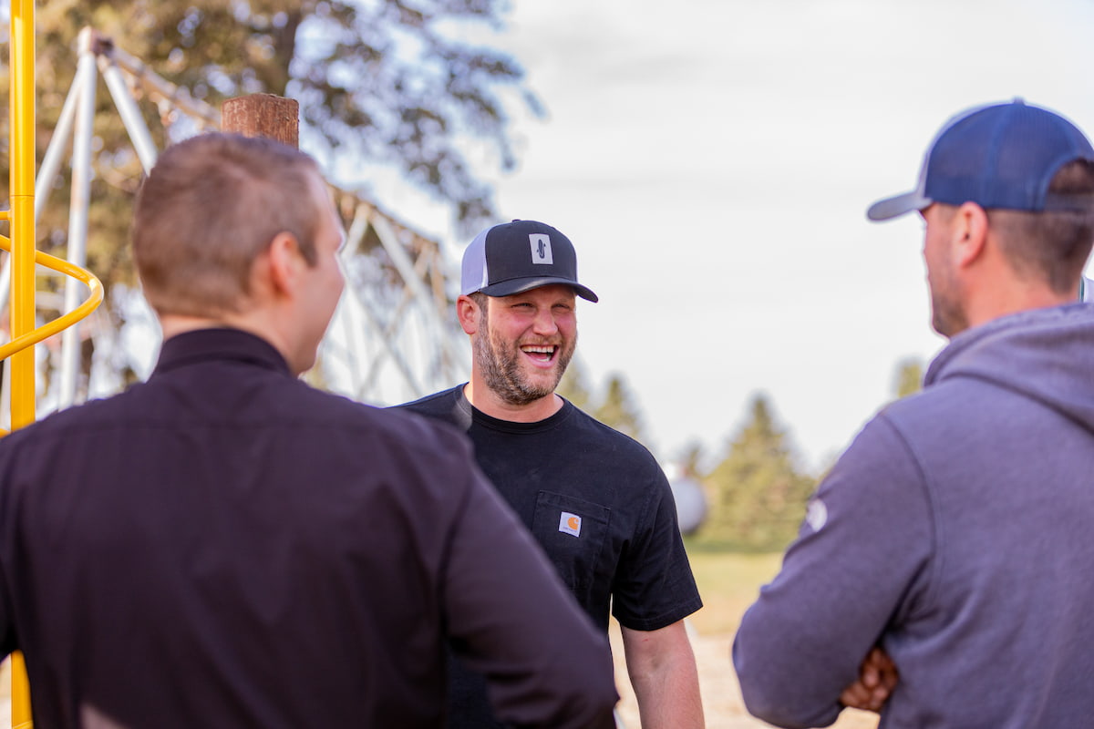 3 men smile and talk while standing outside