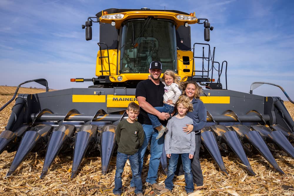 Family poses before combine in harvested corn field